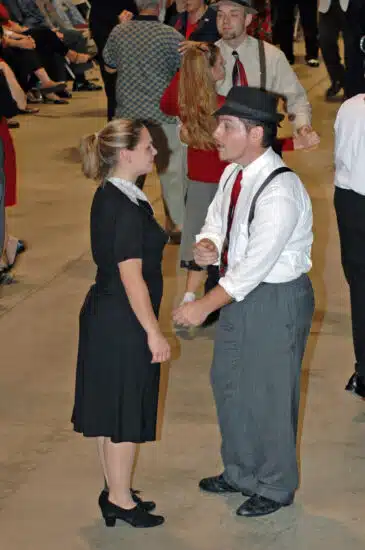 A man and woman in 1940s-style clothing swing dance together on the museum floor while other couples dance in the background during the Trains & Troops event at the Railroad Museum of Pennsylvania.