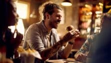 Cheerful man eating burger while gathering with friends in a bar.