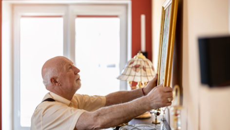 An older man hanging a picture