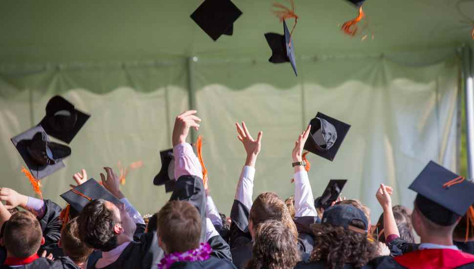 Graduating seniors toss their caps in air.