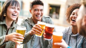 Group of happy multiethnic friends drinking and toasting beer at brewery bar restaurant - Beverage concept with men and women having fun together outside