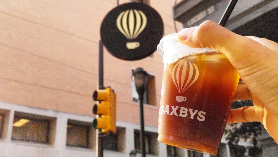 A cup of Saxbys iced coffee held next to a Saxbys sign.