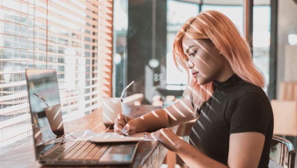 Gen Z woman working at a window sill with laptop