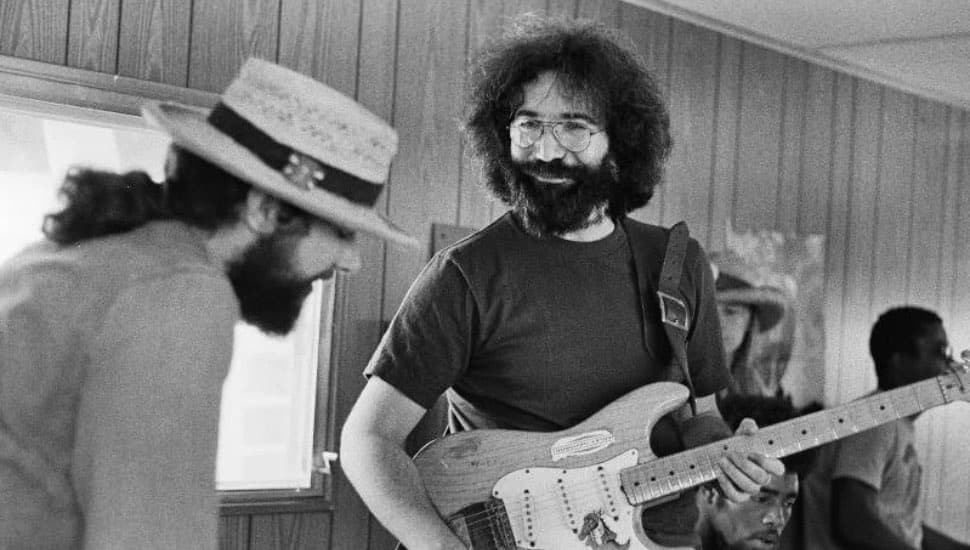 Jerry Garcia holding a guitar while talking to another person