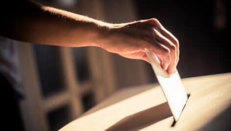 A hand adding a ballot to a ballot box.
