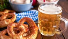 A mug of beer next to pretzels on a table.