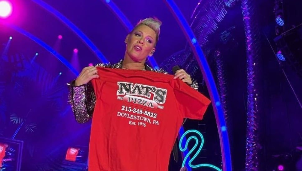 The singer Pink holding a red shit that advertises Nat's Pizzeria