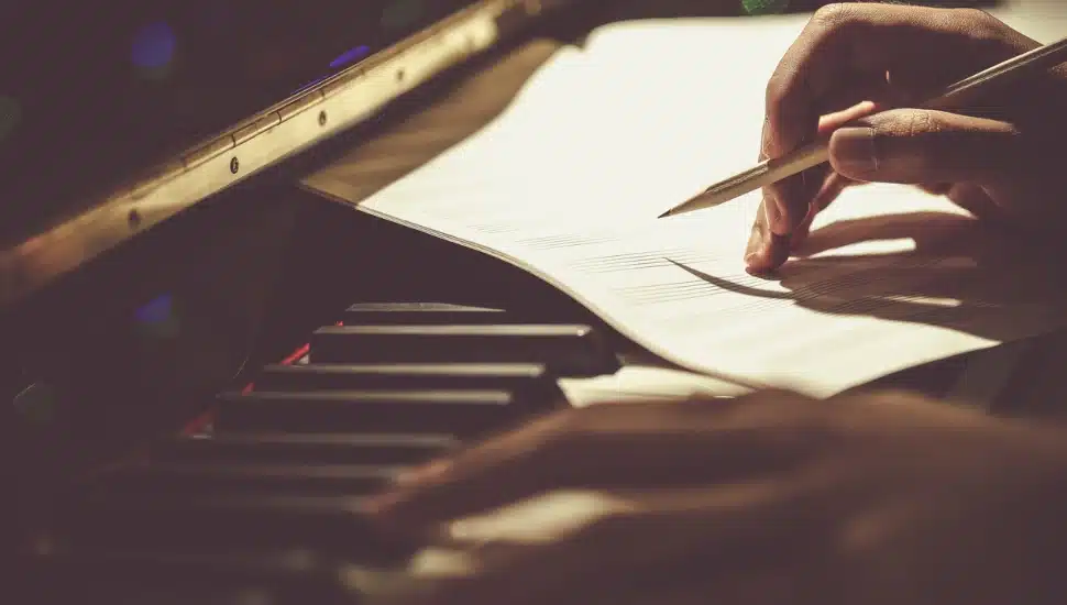 A hand writing on paper atop a piano
