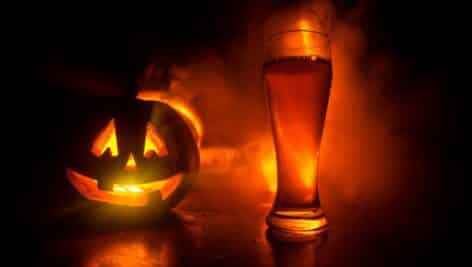 A Jack-o-Lantern with a pint of beer next to it