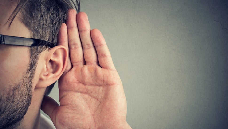 man holds his hand near ear and listens carefully isolated on gray wall background