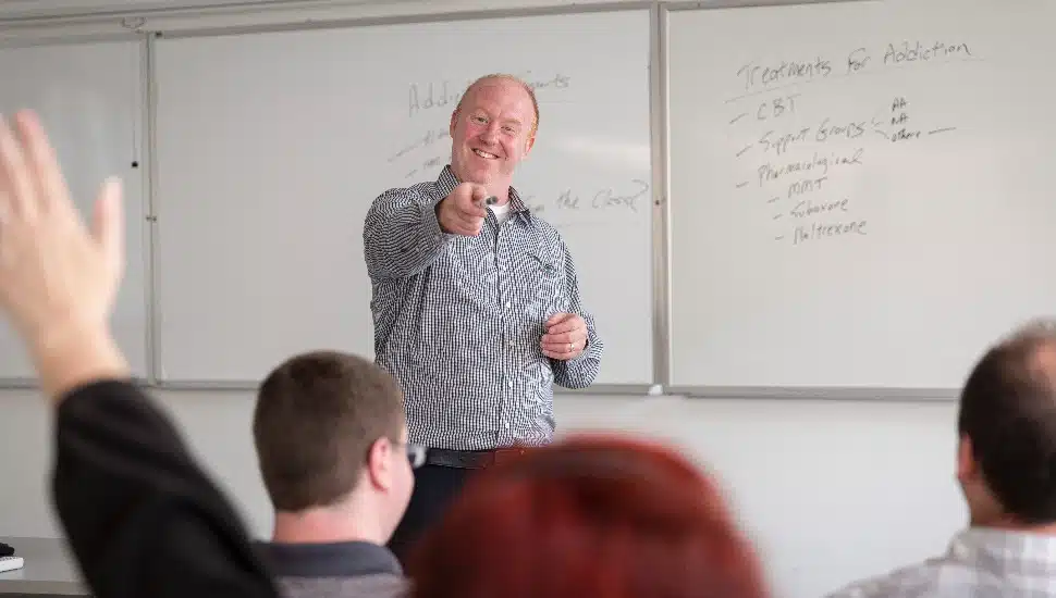 A professor pointing at a student with a raised hand
