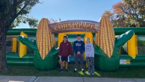 Three attendees stand in front of corn maze inflatables