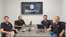 members of the mentomind team sitting at desk in front of plasma tv showing its logo