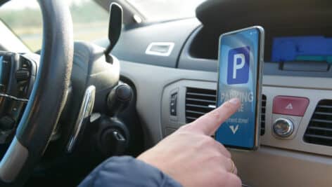 Driver using smartphone app to pay for parking in the paid parking zone in a city