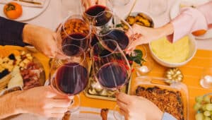 Hands clinking with a glasses filled with red wine at the Thanksgiving dinner table. Celebration, gather, Friendsgiving