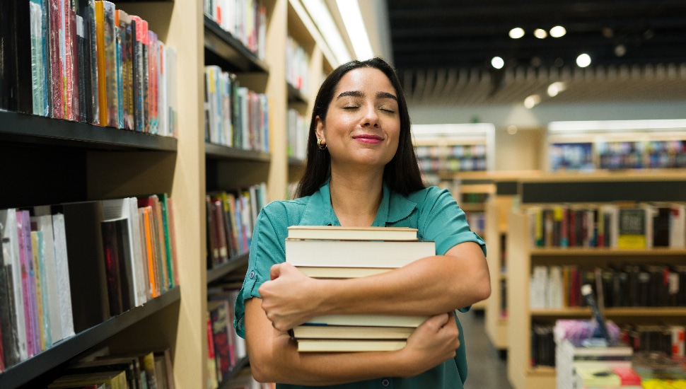 Excited latina woman looking happy carrying a lot of books while buying novels at the bookstore