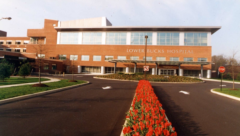 Lower Bucks Hospital exterior in the vantage point of parking lot and flowers in a row