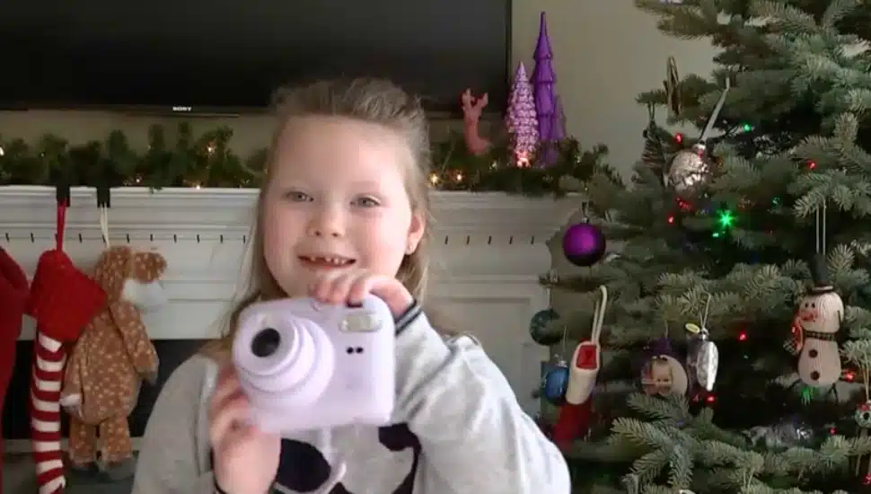 Seven year old Emma smiling with instant camera in front of Christmas tree