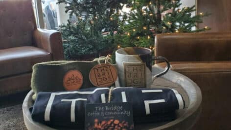 The Bridge Coffee Shop T-shirts and mug on mini table in front of fake Christmas tree