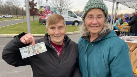 two women at fresh connect market, one holding 100 dollar bill