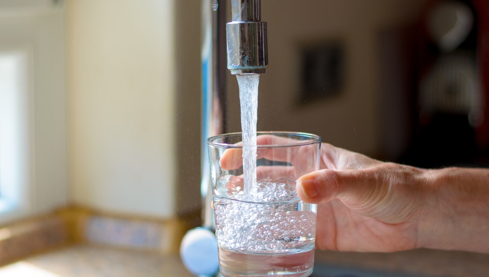 Woman filling a glass of water from a stainless steel or chrome tap or faucet, close up on her hand and the glass with running water and air bubbles