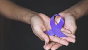 Woman Hand Holding Purple Ribbon, Domestic Violence Awareness Month (October) concept with deep purple awareness ribbon.