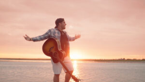 Holdyn Barder in front of water sunset with guitar slung over him