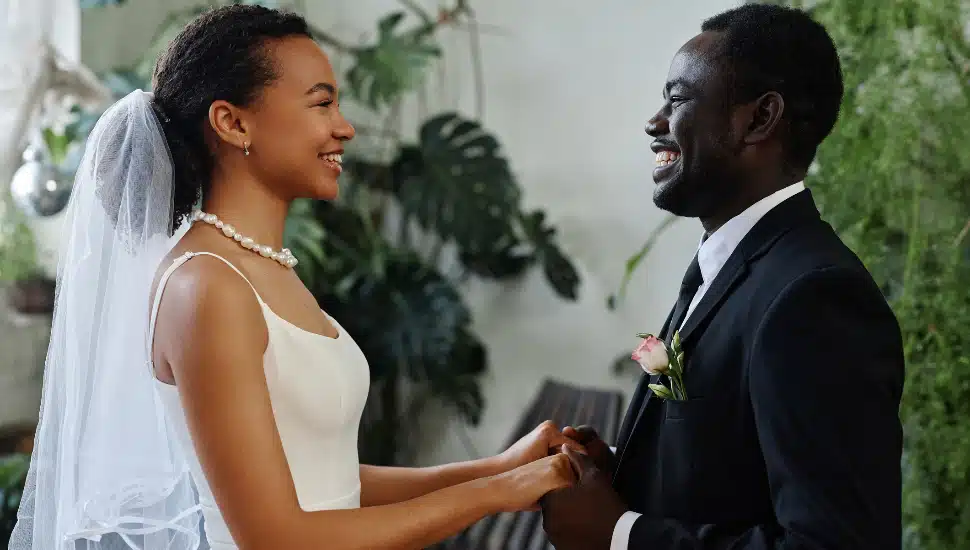 Side view portrait of young black couple as bride and groom looking at each other and holding hands
