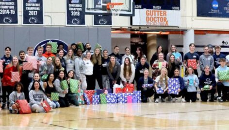 group of student-athletes at Penn State Abington holding wrapped presents in gymnasium