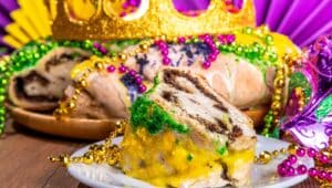 King Cake for Mardi Gras, traditional New Orlean Mardi Gras holiday pastry with plastic baby, with festival masquerade accessories, decor, carnival mask, beads