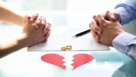 a couple with hands crossed over divorce paper broken heart and wedding rings