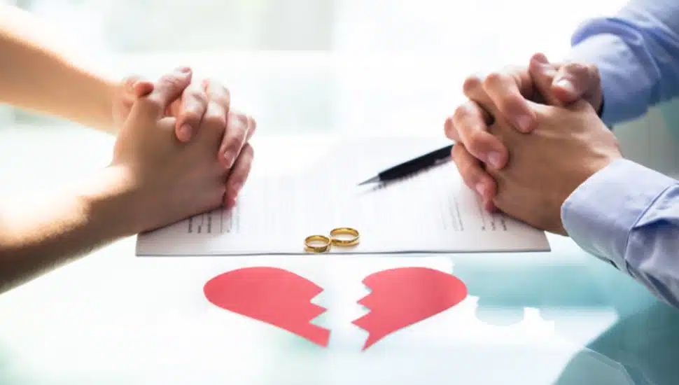 a couple with hands crossed over divorce paper broken heart and wedding rings