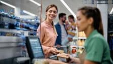 Happy woman paying for groceries at checkout while buying with her family in supermarket.