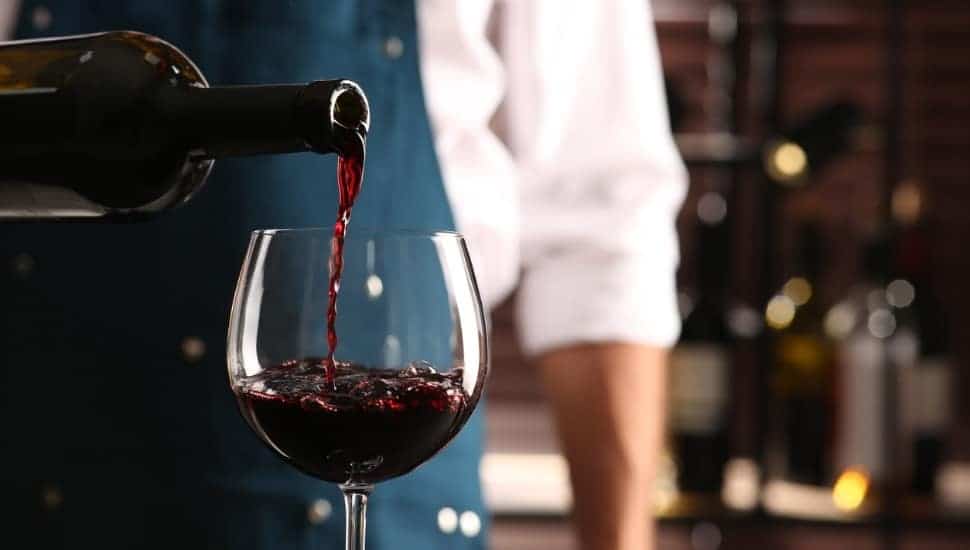 A bartender pouring wine into a glass.
