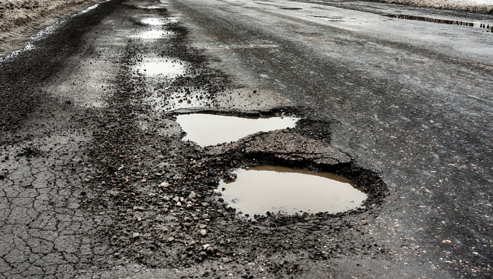 old highway with holes and snow. Landscape road in the potholes in cloudy winter weather. The concept of the absence of timely repair of the highway.