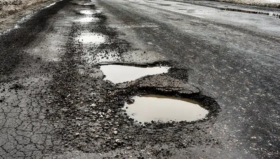 old highway with holes and snow. Landscape road in the potholes in cloudy winter weather. The concept of the absence of timely repair of the highway.