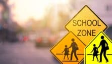 School zone warning sign on blur traffic road with colorful bokeh light abstract background. Copy space of transportation and travel concept. Vintage tone color style.