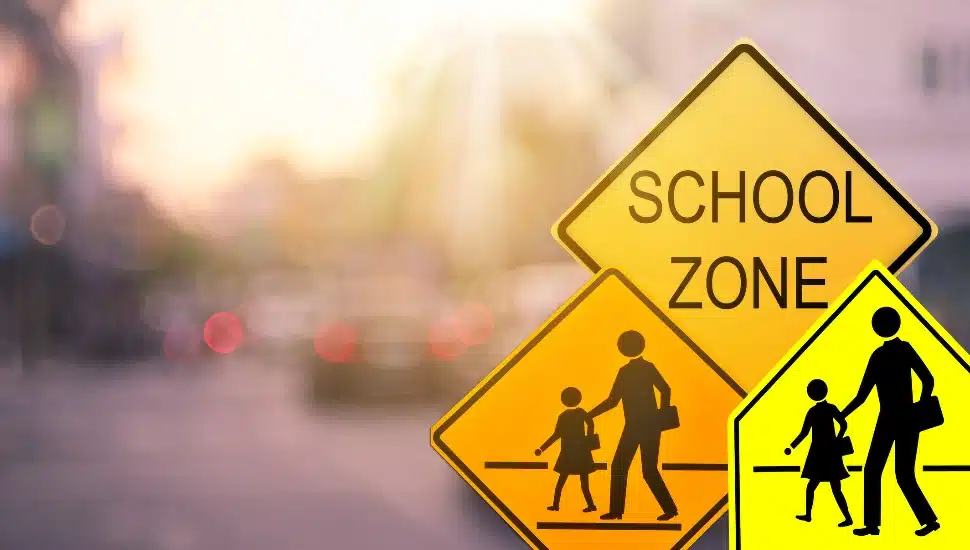 School zone warning sign on blur traffic road with colorful bokeh light abstract background. Copy space of transportation and travel concept. Vintage tone color style.