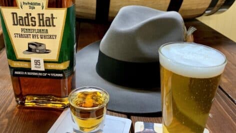 Dad's hat rye whiskey bottle with shot and glass in front of hat on table