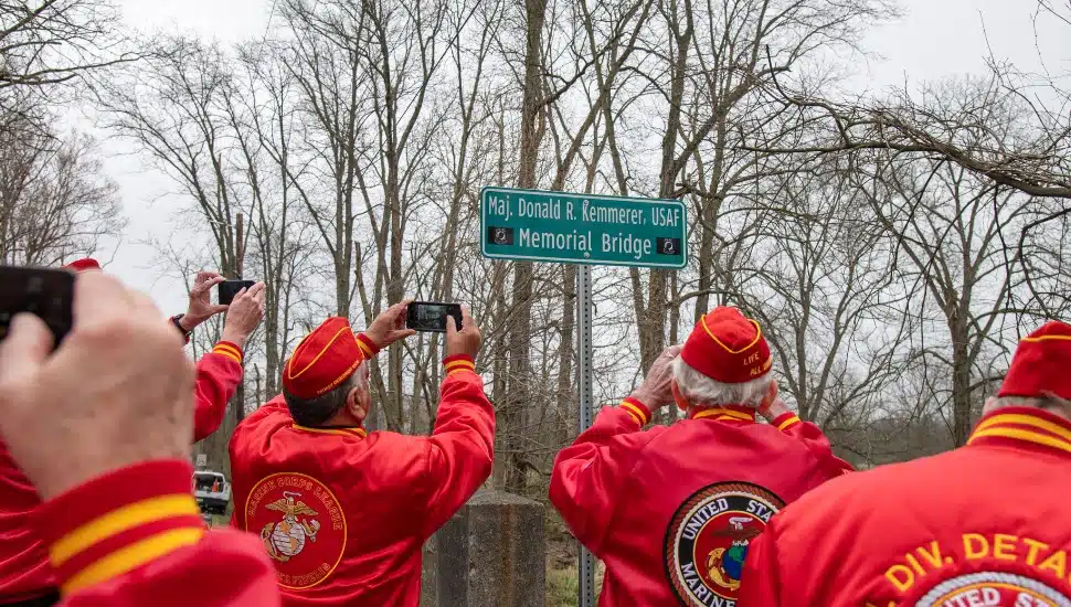 veterans in red jackets and berets taking photo of signage of Donald R. Kemmerer Memorial Bridge