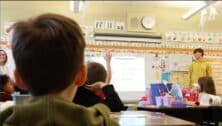 Back of young child's head looking at front of classroom where a high schooler is teaching