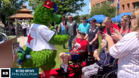 The Phillie Phanatic greets Paul Trumbetas, who wears a red Phillies shirt.