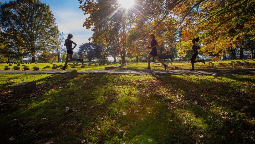 Track athletes running in the graveyard along a stretch of pavement.