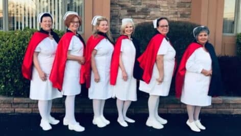 line of nurses in white with white caps red capes