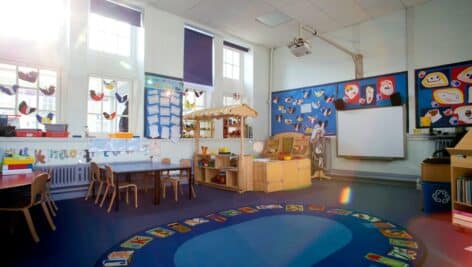 Landscape image of an empty, nursery classroom. there is a rug in the middle of the room.