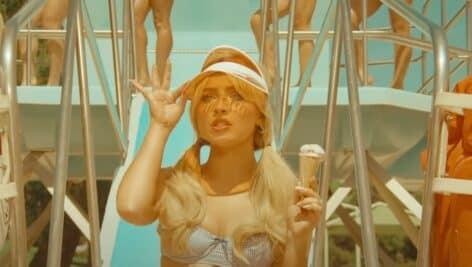 Sabrina carpenter sitting at edge of slide in a visor and swimsuit holding ice cream cone in Espresso music video