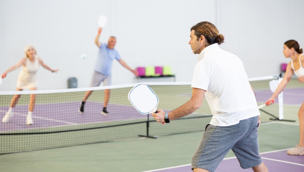 Rear view of man in sportswear playing pickleball tennis on court. Racket sport training indoors