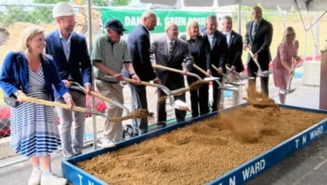 Group of people holding shovels in front of box of sand