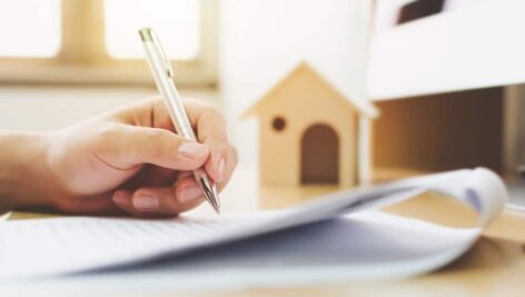 Close up hand of man signing signature loan document to home ownership. Mortgage and real estate property investment