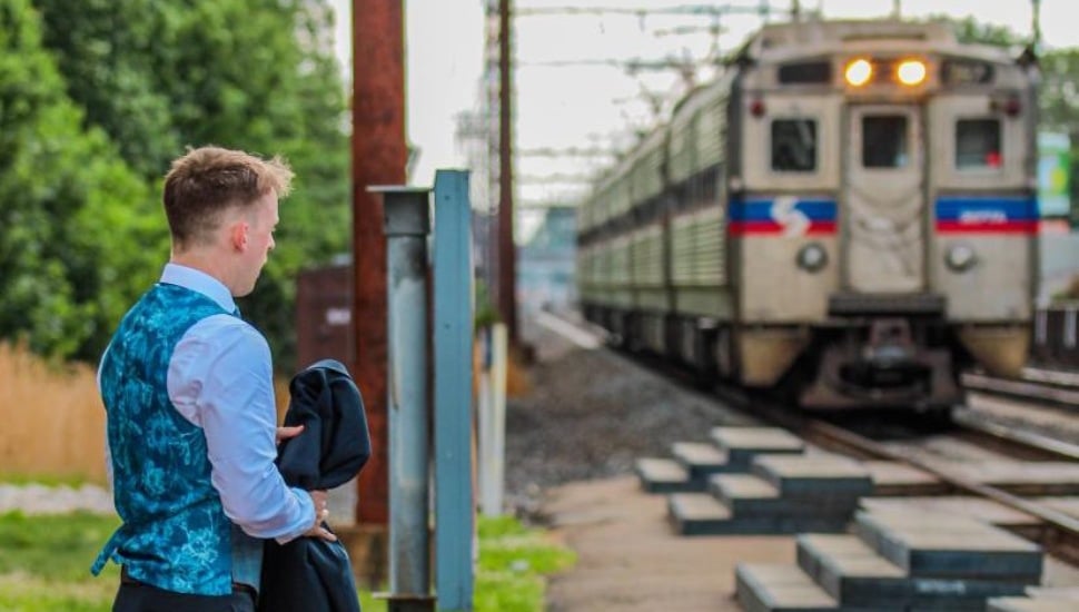 A man in formal attire waits at the regional rail train platform as a train pulls into the station.